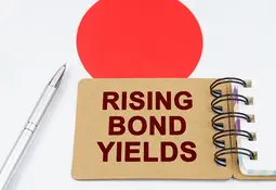 Notizkarte mit der Aufschrift „Rising Bond Yields“ vor Japans Nationalflagge – Symbol für steigende Anleiherenditen und Zinsrisiken.