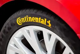 Nahaufnahme eines Autoreifens mit Continental-Schriftzug, daneben ein Teil der roten Fahrzeugkarosserie