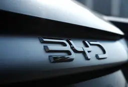 Detailaufnahme eines metallischen BYD-Logos auf der dunklen Rückseite eines modernen Autos, Fokus auf die glänzende Oberfläche und das Fahrzeugdesign.